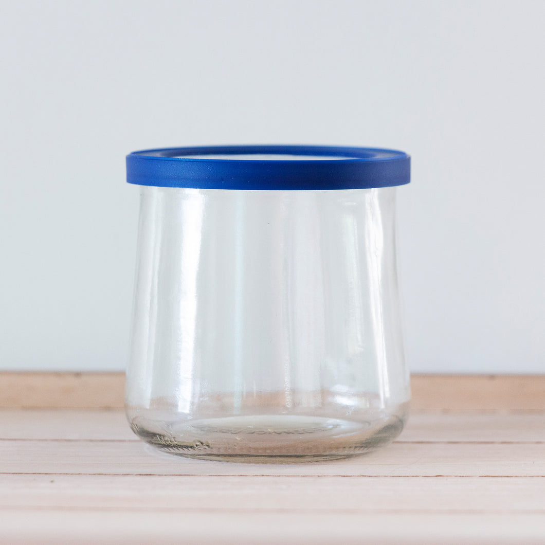 A clear, empty, unlabeled Oui by Yoplait yogurt jar with a blue lid.