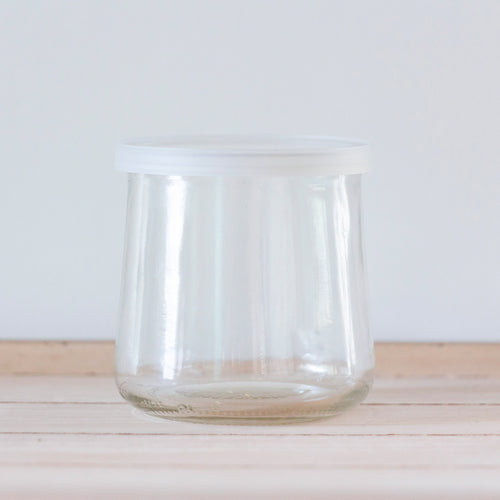 A clear, empty, unlabeled Oui by Yoplait yogurt jar with a clear lid.